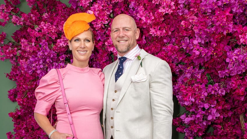 Zara Tindall wearing a pink dress and orange fascinator next to Mike Tindall in a beige suit