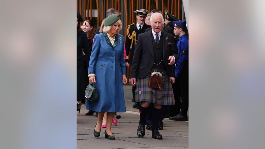 King Charles in a kilt walking next to Queen Camilla in a blue coatdress