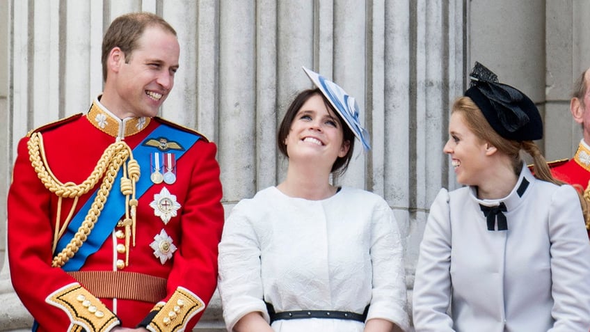 Prince William in a red uniform smiling next to his cousins Princess Eugenie and Princess Beatrice.