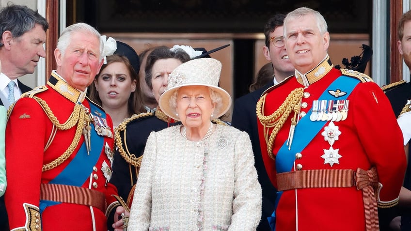 Queen Elizabeth wearing an ivory coat dress standing in between King Charles and Prince Andrew wearing matching red uniforms.