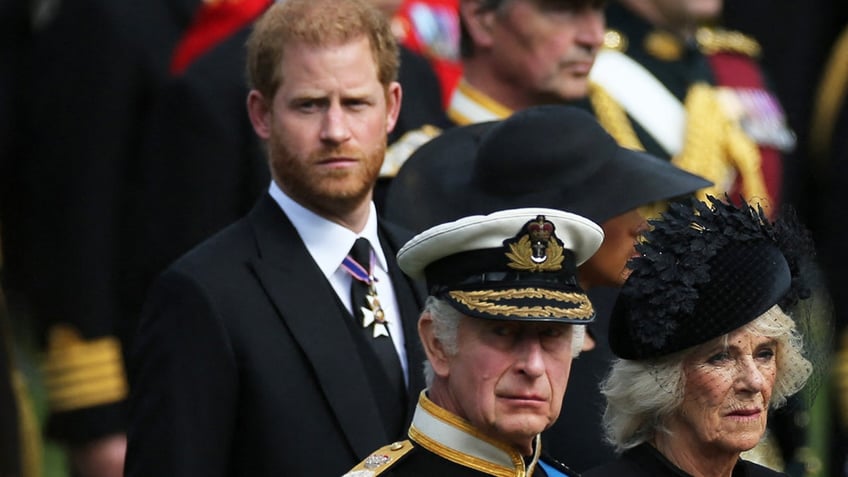 Prince Harry looking to the side as a somber King Charles and Queen Camilla look ahead.