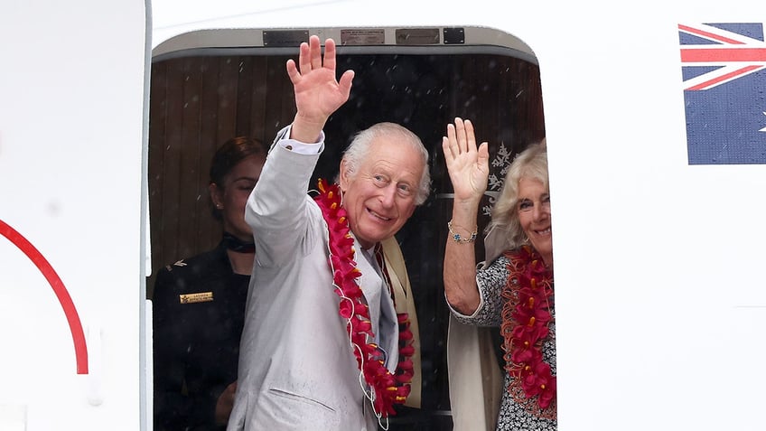 King Charles and Queen Camilla waving from a plane.