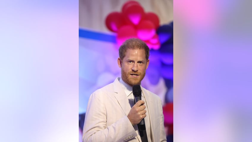 Prince Harry speaking to a mic wearing an off-white suit