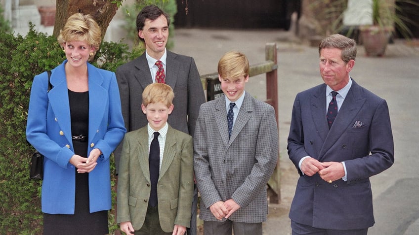 Princess Diana in a blue blazer and black dress standing next to her two sons and Prince Charles as they wear suits