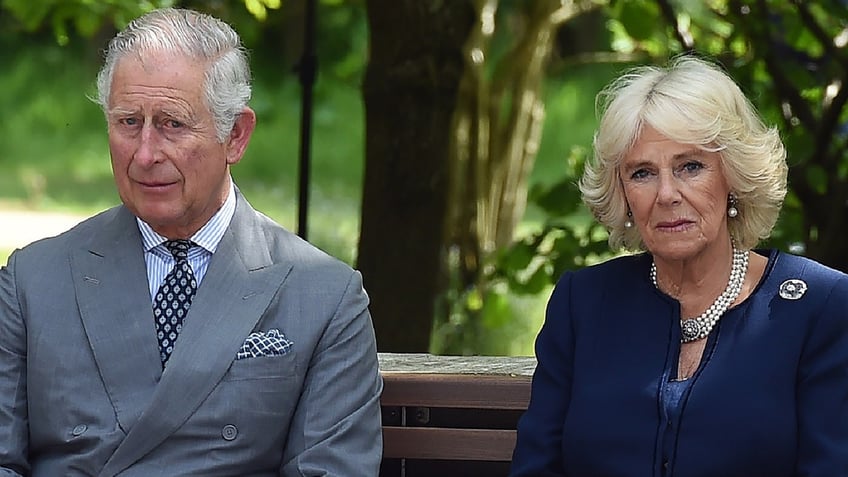 King Charles and Queen Camilla sitting next to each other outdoors looking serious