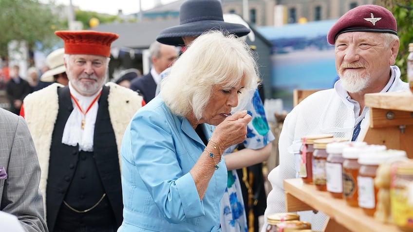 Queen Camilla in a blue dress tasting honey.