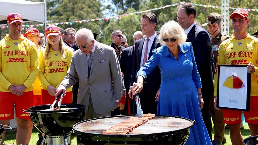 King Charles and Queen Camilla wearing sunglasses and grilling hot dogs.