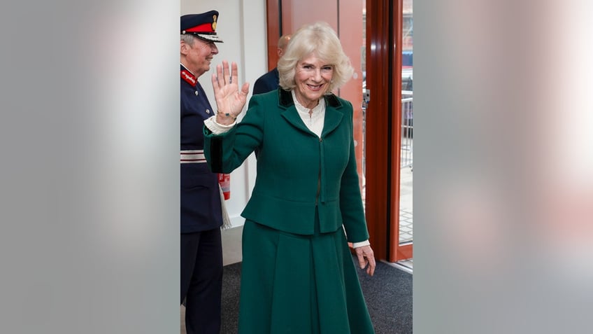 Queen Camilla in a hunter green suit waving