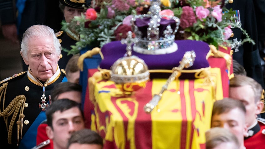 King Charles looking sad next to his mothers coffin