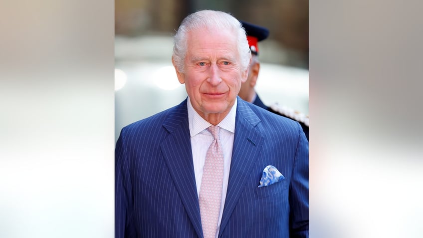 King Charles wearing a blue suit and a dinosaur-printed tie.