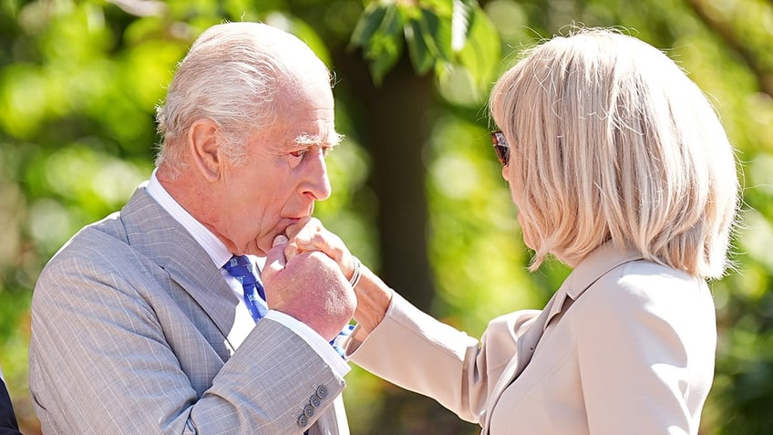 King Charles kissing first lady Macron on the hand.