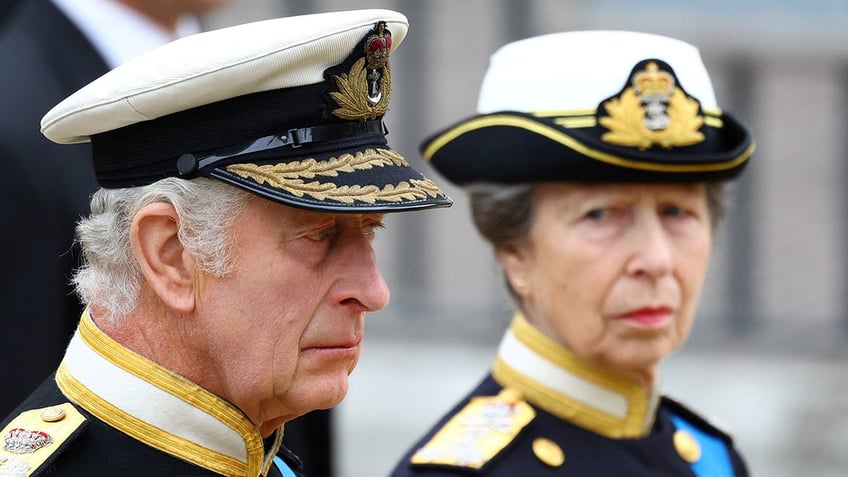 Princess Anne looking at King Charles as they both wear matching uniforms and look somber.