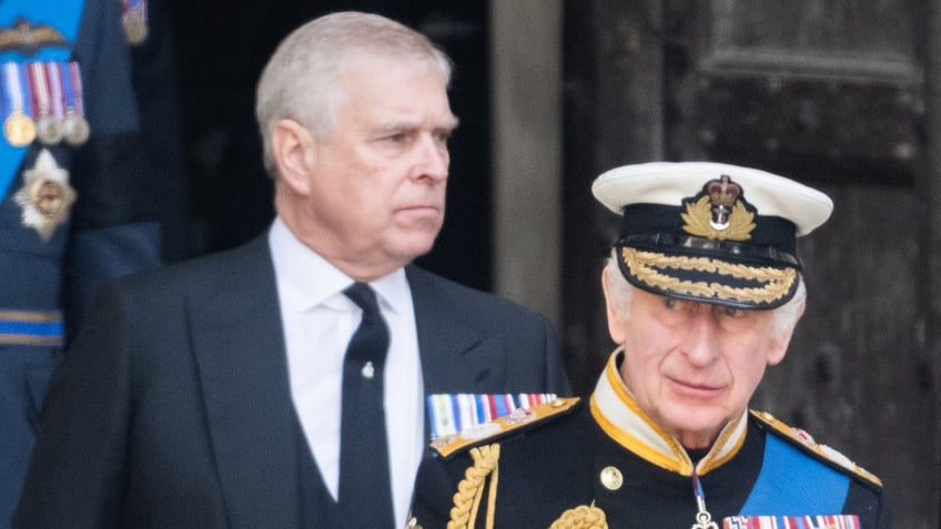 King Charles in uniform walking ahead of Prince Andrew in a suit.