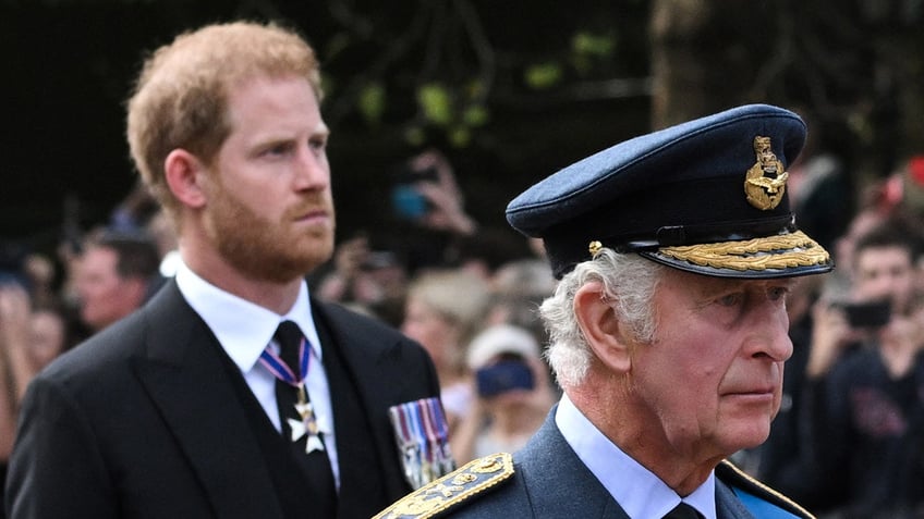 Prince Harry looking somber walking behind a stern King Charles in uniform