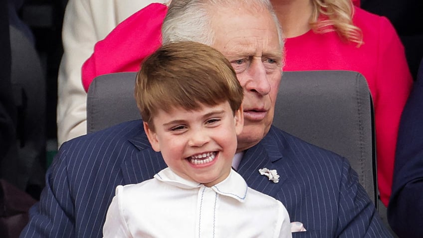 A smiling Prince Louis sitting on his grandfather King Charles lap.