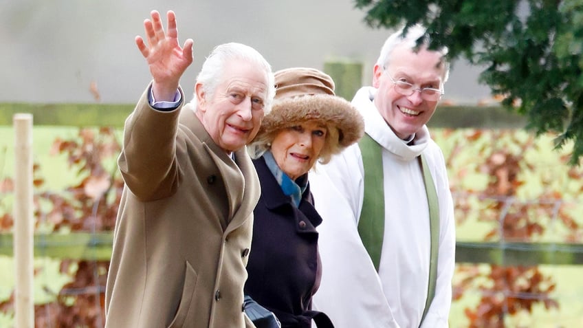 King Charles waving next to Queen Camilla and a priest