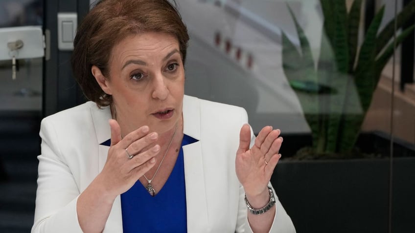 Kosovo's foreign minister and deputy prime minister Donika Gërvalla-Schwarz gestures with both hands and wears a white blazer and blue shirt during an interview in Warsaw, Poland.