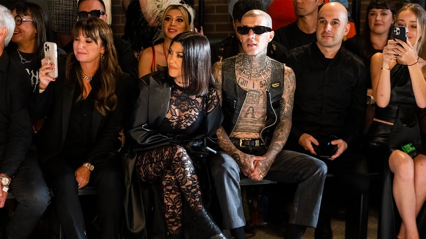 Kourtney Kardashian and Travis Barker sit front row at a fashion show.