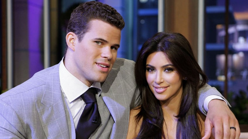 Kris Humphries in a grey suit and black tie puts his arm around Kim Kardashian