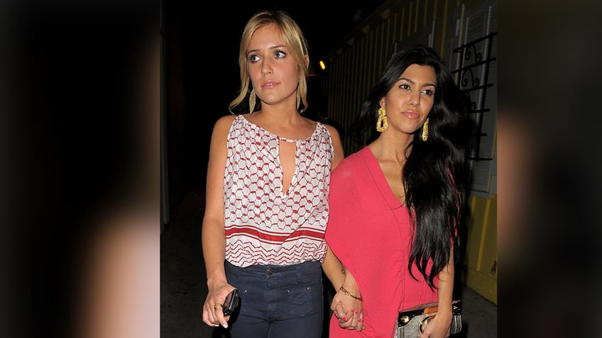 Kristin Cavallari in a patterned top and jeans walks hand-in-hand with Kourtney Kardashian in a pink dress