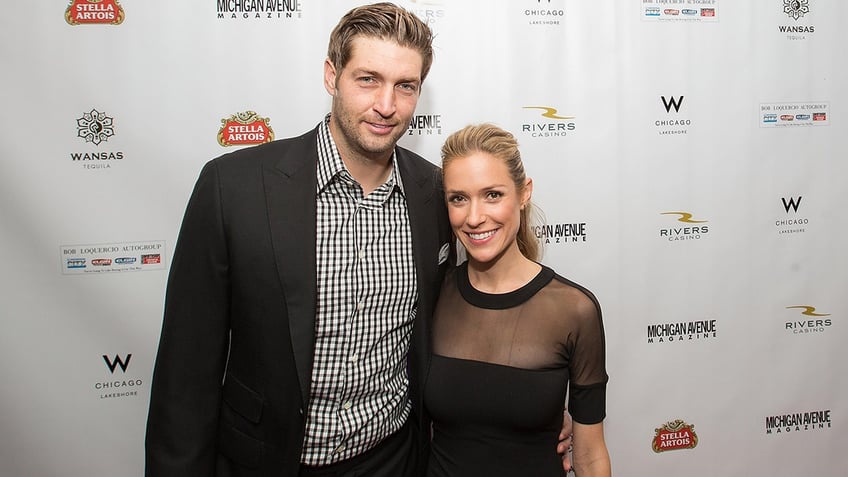 Jay Cutler in a black suit and checkered shirt smiles on the carpet with Kristin Cavallari in a black dress with a mesh top