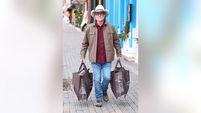 kurt russell walking down the sidewalk in aspen carrying two large shopping bags