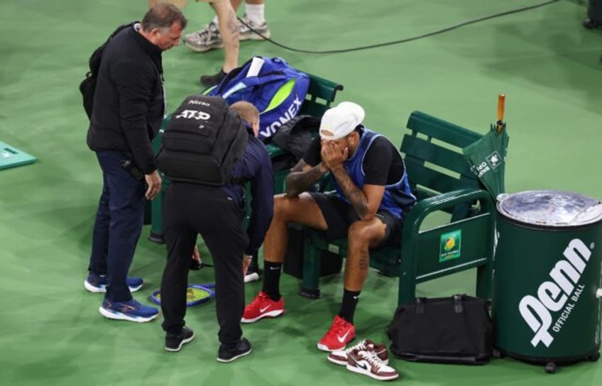 A devastated Nick Kyrgios is surrounded by trainers after retiring from his first-round ma