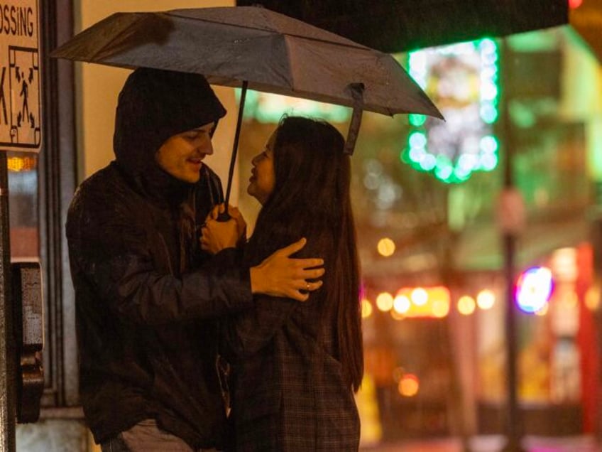 PASADENA, CA - FEBRUARY 4, 2024: A couple share space and an umbrella at a cross walk as heavy rain fall off Colorado Boulevard on February 4, 2024 in Pasadena, California. The heavy rain is supposed to last until Tuesday and cause flooding in many Southern California areas.(Gina Ferazzi / …