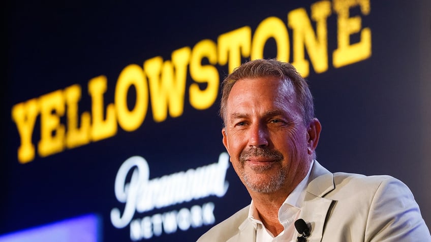 Kevin Costner sitting in front of a Yellowstone sign