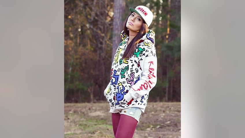 Mei Haskell in hoodie and hat posing near forest