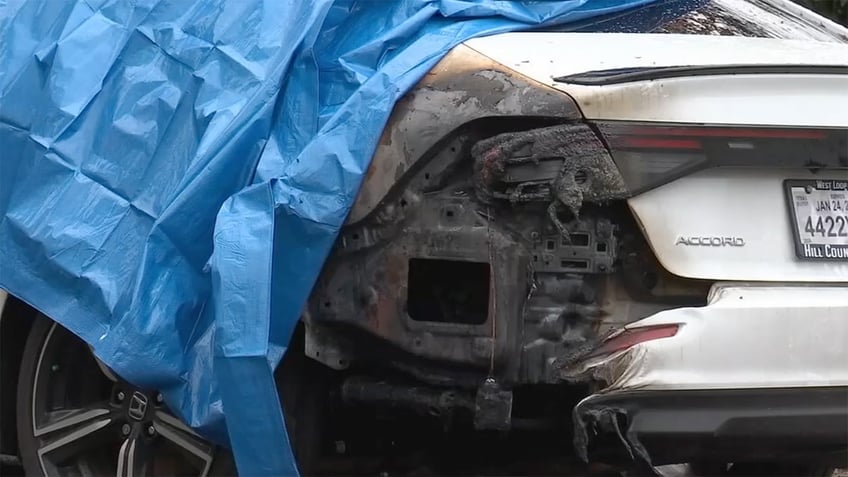 Blue tarp draped over a white car with a burned bumper