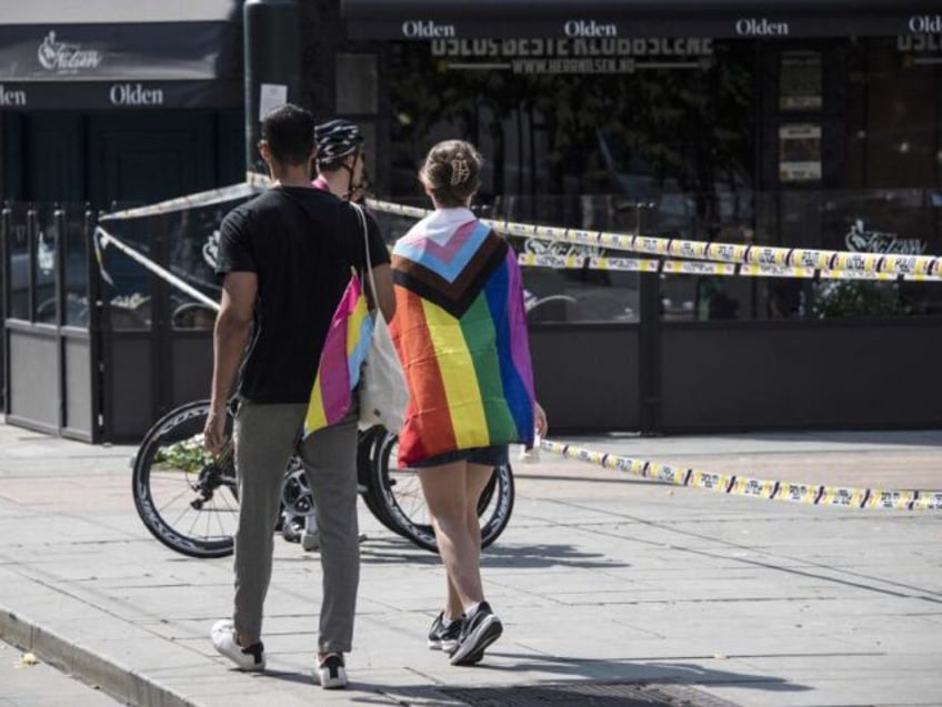 People with a progress and a pansexual flag walk by a crime scene on June 25, 2022, in the