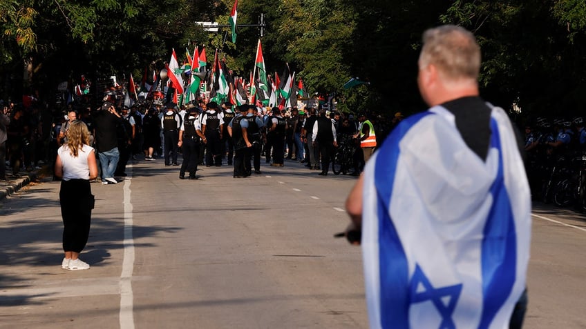 A person covers themselves with an Israeli flag while looking at demonstrators during a protest in support of Palestinians in Gaza, amid the Israel-Hamas conflict