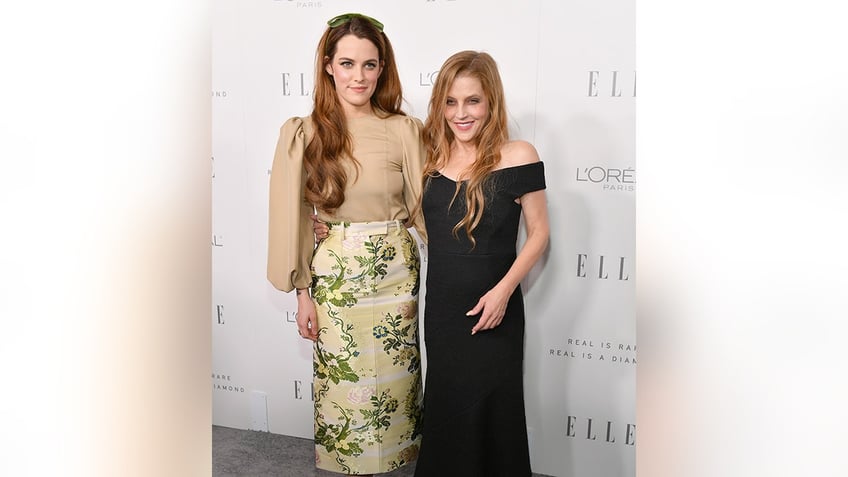 Riley Keough in a tan shirt and green floral skirt stands on the carpet with mother Lisa Marie Presley in a black bodycon dress