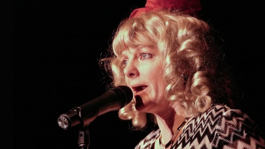 Alison Arngrim speaking to a mic with a Nellie Oleson wig