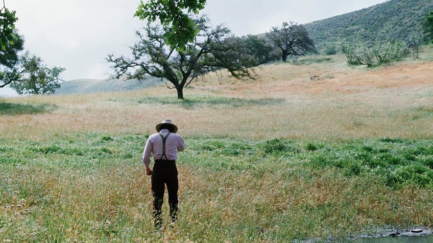 Michael Landon standing in a field looking away from the camera