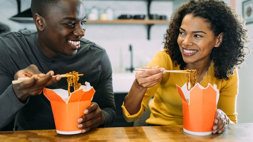 Man and woman eating chinese takeout food in carton boxes at home.