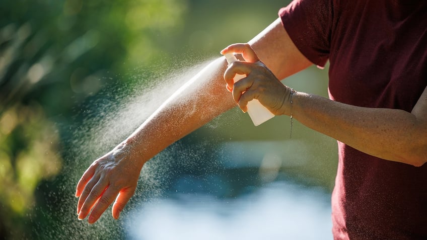 a person applies insect repellent to their arm