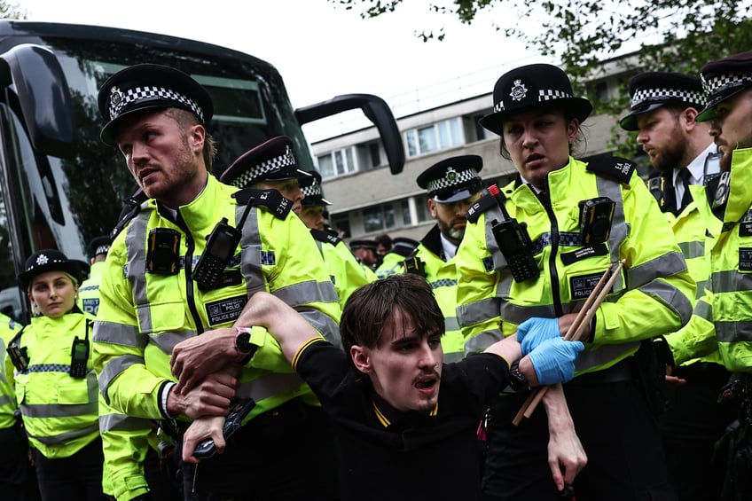 TOPSHOT - Metropolitan Police officers (MET) escort away a protester taking part in a gathering around a bus reportedly waiting to remove migrants and asylum seekers from a hotel in Peckham, south London, as they block it from transporting them to the Bibby Stockholm barge in Portland, Dorset, south-west England, on May 2, 2024. Protesters in London tried Thursday to prevent the removal of migrants from their temporary accommodation, as the UK government began detaining people before controversial deportation flights to Rwanda start. (Photo by HENRY NICHOLLS / AFP) (Photo by HENRY NICHOLLS/AFP via Getty Images)