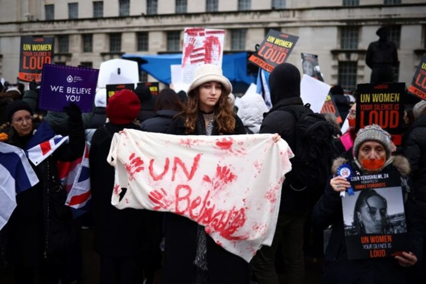 Demonstrators hold posters reading "UN Women, your silence is loud" along with a red paint-stained sheet reading "UNbelievable"