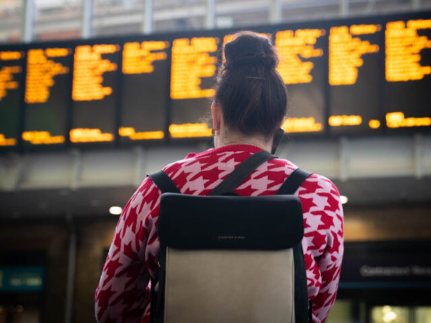 Passengers look at the departure board at Kings Cross station in London, as members of the