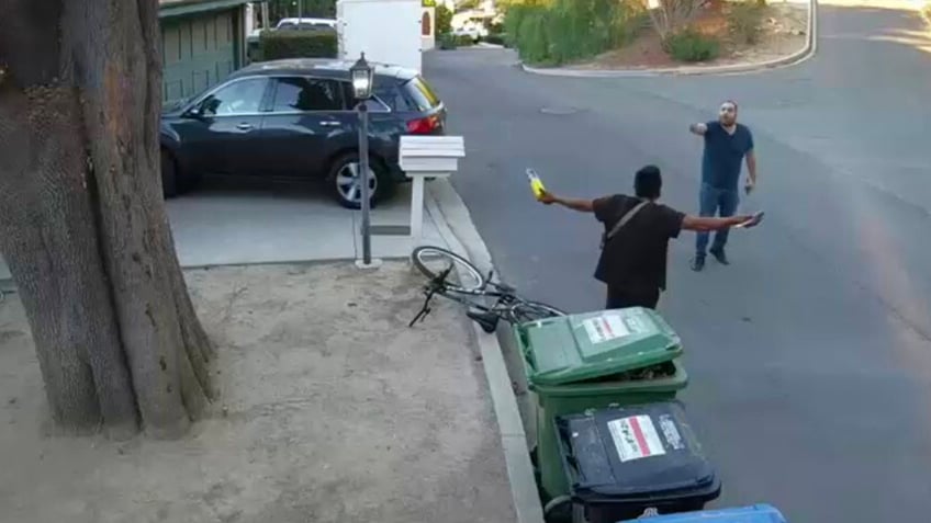 a man holding what appears to be a fuel tank and blowtorch nozzle as a homeowner confronts him