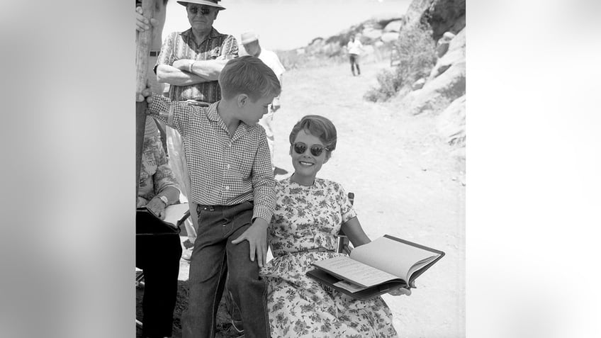 Jon Provost sitting next to June Lockhart who is wearing a floral dress and holding a script.