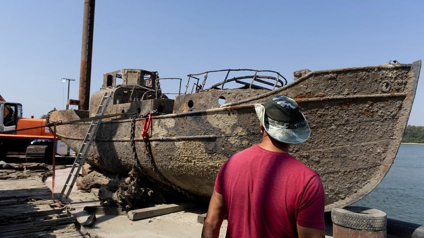 A fisherman inspects a sunken German warship from World War II, recently recovered from the Danube river after being exposed due to low water levels caused by drought and extreme heat, in Prahovo