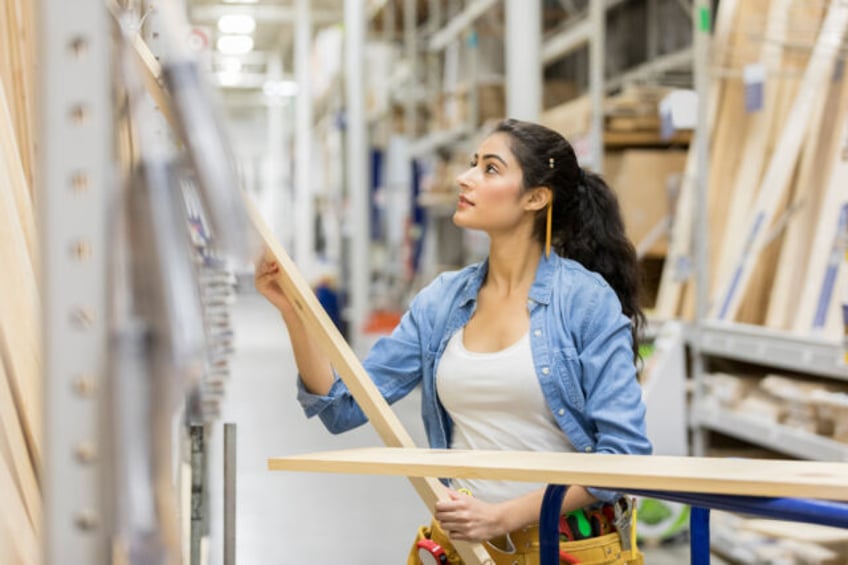 Confident young Middle Eastern female home improvement store employee loads wooden planks