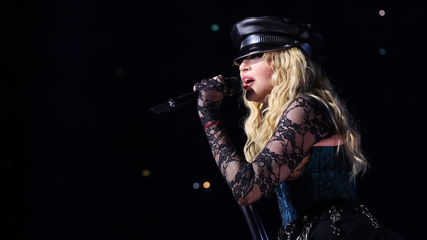 Madonna in a lace longsleeve top and conductor hat sings on stage