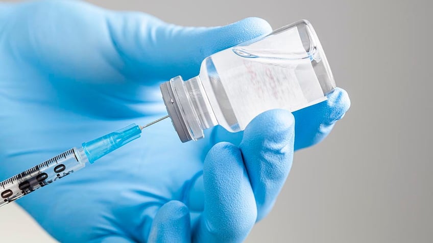 Close upshot of healthcare professional sucking liquid medication or vaccine into a syringe from a glass vial with suction cap.