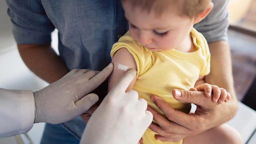 Doctor putting a patch on little boy's shoulder after vaccination.