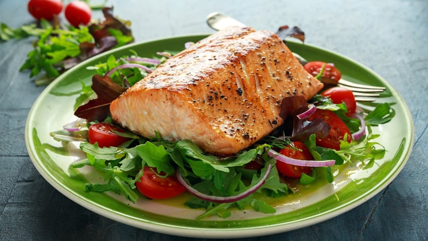 A piece of salmon is on top of salad on a plate.