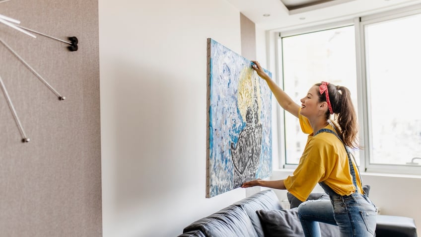 A woman hanging wall art in her home